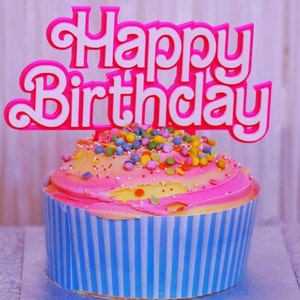May include: A frosted cupcake with pink and yellow icing, topped with colorful sprinkles and a pink and white "Happy Birthday" cake topper. The cupcake is in a blue and white striped liner.