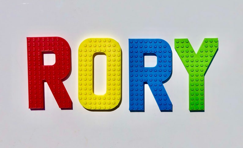 May include: Colorful letters spelling "RORY" in red, yellow, blue, and green. The letters are designed to resemble toy building blocks, with a textured surface of small circular studs. The letters are arranged on a white background.