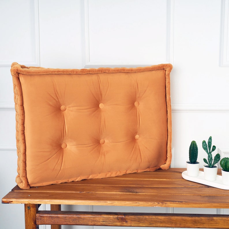 Puede incluir: Un coj&iacute;n grande, rectangular, de terciopelo naranja con botones. El coj&iacute;n est&aacute; sobre un banco de madera.