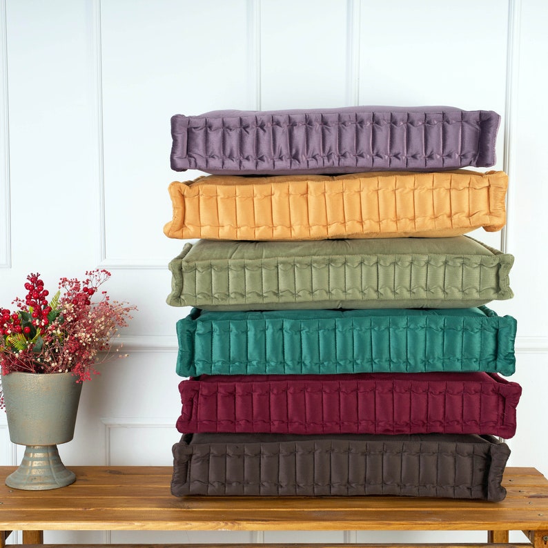 Puede incluir: Una pila de seis cojines de suelo en varios colores, incluyendo morado, amarillo, verde, verde azulado, burdeos y marr&oacute;n. Todos los cojines est&aacute;n acolchados y tienen un dise&ntilde;o capiton&eacute;.