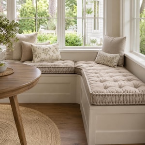 Puede incluir: Un banco de ventana en forma de L con cojines beige capitoné y bordes ribeteados. El área de asiento incluye dos cojines cuadrados beige grandes, un cojín rectangular beige y dos cojines rectangulares más pequeños con estampado floral.