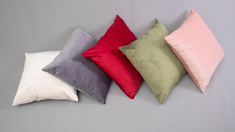 May include: Five decorative throw pillows in various colors and textures. The pillows are arranged in a row on a gray surface. The pillows are made of velvet and have a soft, plush feel.