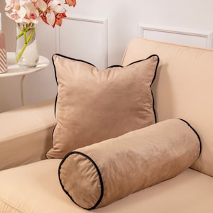 Pu&ograve; includere: Un cuscino in velluto beige con un bordo nero e un cuscino di supporto in velluto beige abbinato con un bordo nero.