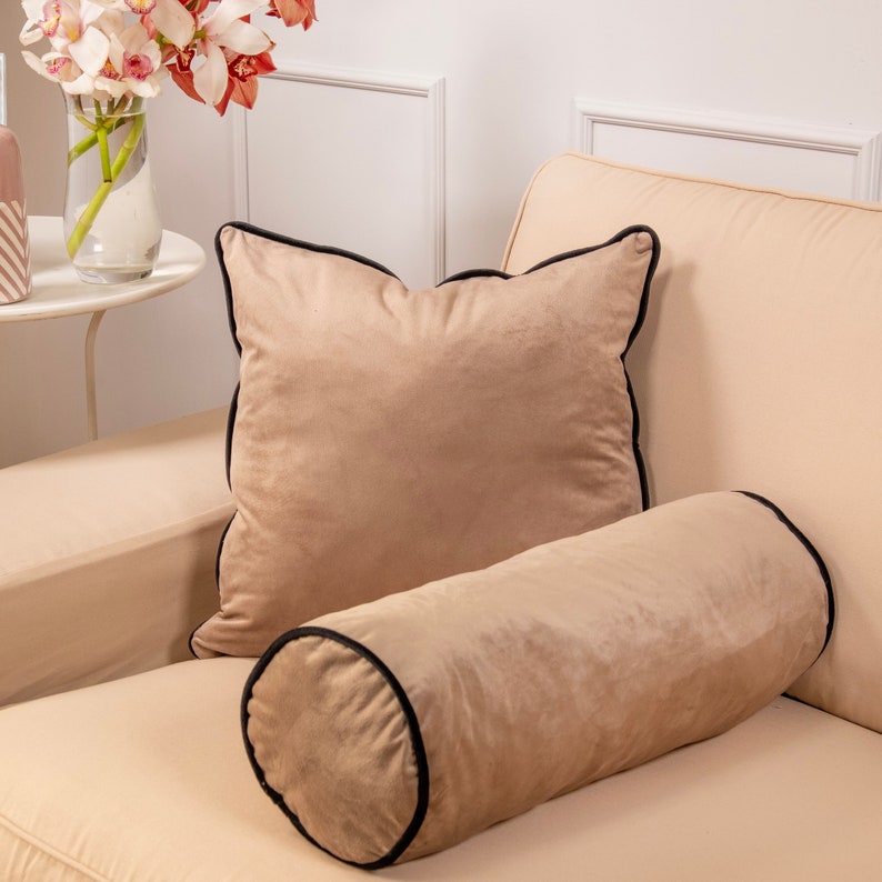Pu&ograve; includere: Un cuscino in velluto beige con un bordo nero e un cuscino di supporto in velluto beige abbinato con un bordo nero.