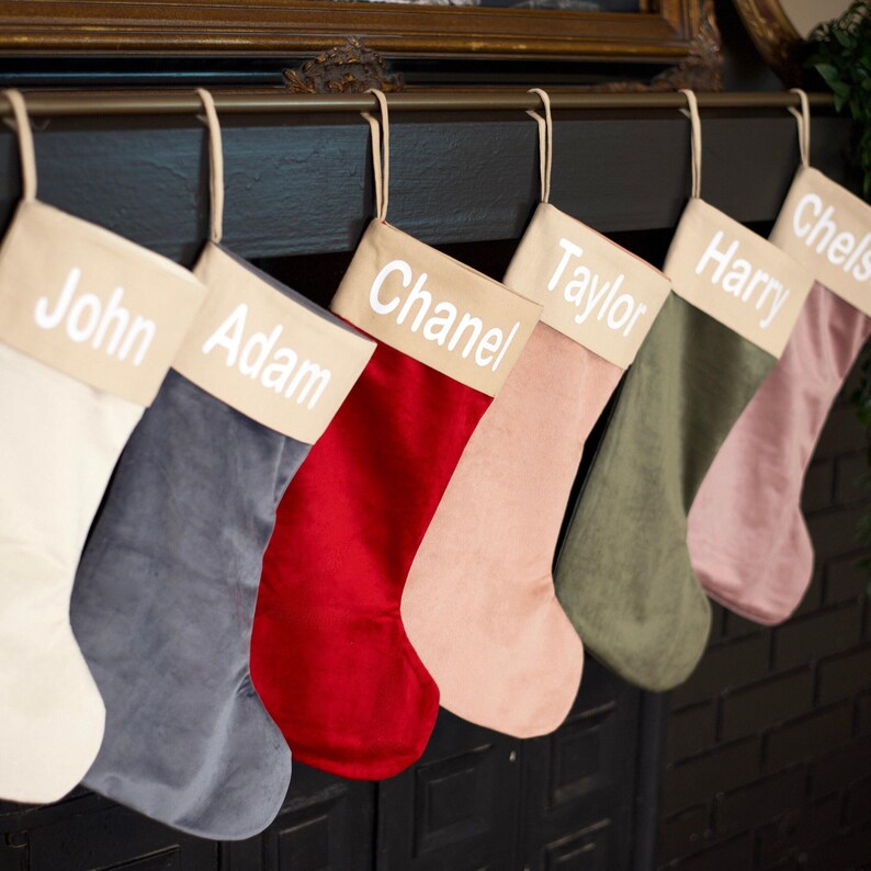 A row of colorful Christmas stockings with names on them, hanging on a fireplace mantel.