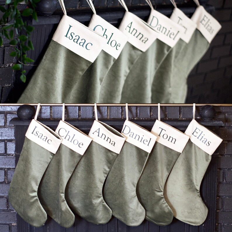 A collection of green stockings with names of family members or friends printed on them, hanging on a wall or mantle.