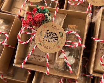 May include: A rectangular cardboard gift box containing a small packet of Kurukahveci Mehmet Efendi Turkish coffee and a glass vial with a cork stopper filled with small stones, tied with red and white twine and a Happy Holidays tag.