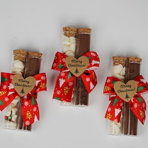 May include: Three glass tubes filled with white and brown chocolate pieces, tied with red and green ribbon bows and a brown heart-shaped tag that says "Merry Christmas!"