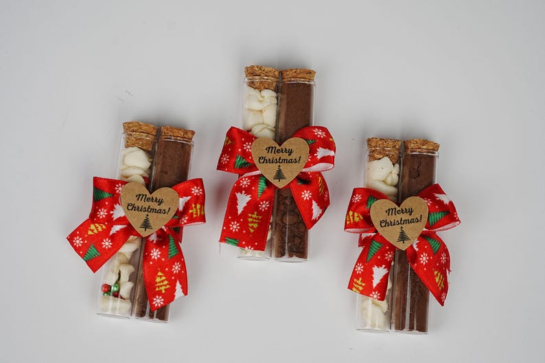 May include: Three glass tubes filled with white and brown chocolate pieces, tied with red and green ribbon bows and a brown heart-shaped tag that says "Merry Christmas!"