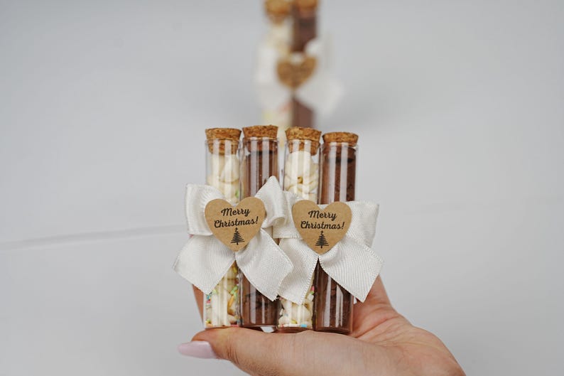 May include: Four glass test tubes filled with white and brown sprinkles, tied with white ribbon and a brown heart-shaped tag that says "Merry Christmas!"