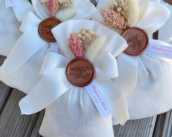 May include: White fabric pouches with a brown wax seal and dried flowers. The pouches have a white ribbon and a tag that says "Meghan & Adam 5/25/24".
