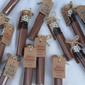 May include: Clear glass tubes filled with brown powder, some with decorative silver beads and cork stoppers. Each tube has a small brown tag with the words "Merry Christmas" or "Baby it's Cold Outside".