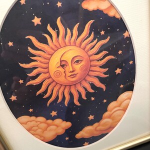 May include: A framed circular print featuring a golden sun with a human face partially eclipsed by a crescent moon. The celestial scene is set against a dark navy blue night sky filled with small yellow stars and fluffy orange clouds.