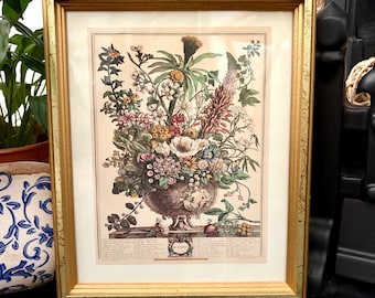May include: A framed botanical print featuring a colorful arrangement of various flowers in a decorative urn. The artwork is encased in a gold-toned frame with a distressed finish and includes a detailed legend with text at the bottom of the print.