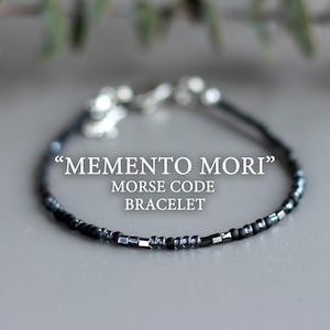 Könnte beinhalten: Ein Armband aus schwarzen und silbernen Perlen mit einem Verschluss. Das Armband besteht aus kleinen, runden Perlen und trägt den Text "MEMENTO MORI" MORSE CODE BRACELET.