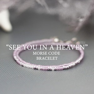 Puede incluir: Un delicado brazalete de cuentas moradas y plateadas con el mensaje "SEE YOU IN A HEAVEN" en código Morse. El brazalete es un regalo considerado para alguien que ha perdido a un ser querido.