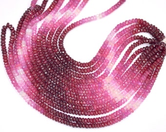 May include: A strand of faceted ruby beads in various shades of pink and red. The beads are arranged in a graduated pattern, with the darkest red beads at the bottom and the lightest pink beads at the top.