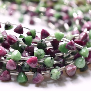 May include: A strand of green and pink gemstone beads, each bead is faceted and shaped like a triangle. The beads are strung on silver wire.