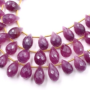 Könnte beinhalten: Eine Strähne aus facettierten, violetten Edelsteinperlen in Tropfenform. Die Perlen sind auf goldfarbenem Draht aufgefädelt.