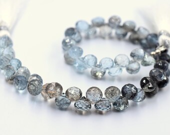 May include: A strand of faceted aquamarine beads in a gradient of light blue to dark gray. The beads are strung on a silver wire and have a tassel at each end.