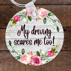 May include: Round white key chain with a floral design and the text "My driving scares me too!"