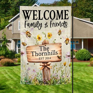May include: A garden flag with the words "WELCOME Family & Friends" in black script. A wooden sign reads "The Thornhills EST 2014". The flag features bees, flowers, and a wooden post with a bow.