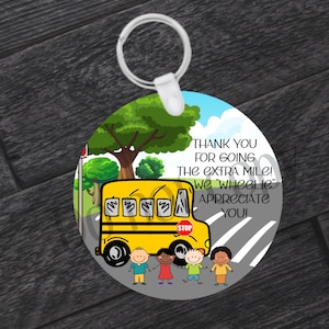 May include: A yellow school bus with a stop sign, surrounded by four children, on a round keychain with the text "Thank you for going the extra mile! We 'wheeliе' appreciate you!"