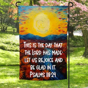 May include: A colorful garden flag with a painted sunrise and the text "THIS IS THE DAY THAT THE LORD HAS MADE LET US REJOICE AND BE GLAD IN IT. PSALMS 118:24".
