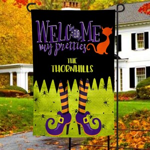 May include: A black and green Halloween garden flag with the text "Welcome my pretties The Thornhills" and a witch's legs with purple shoes and orange and black striped stockings.