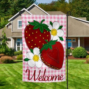 Può includere: Una bandiera da giardino con un motivo a quadri rossi e bianchi, raffigurante un disegno di fragole e la scritta "Welcome". Le fragole hanno foglie verdi e fiori bianchi con centri gialli. La bandiera è esposta in un giardino.