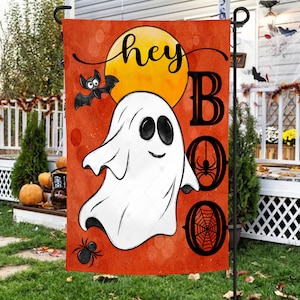 以下が含まれることがあります： オレンジと黄色のハロウィーンのガーデンフラッグ。白い幽霊、コウモリ、クモ、そして「hey boo」の文字が書かれています。