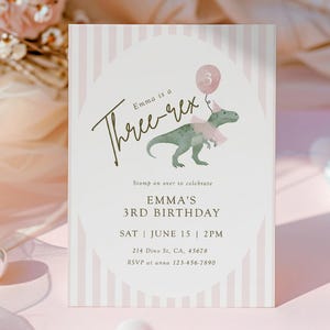 May include: A birthday invitation with a pink and white striped background. The invitation features the text "Emma is a Three-rex" and a watercolor illustration of a green dinosaur wearing a party hat and a pink bow. The invitation includes the date, time, and location.