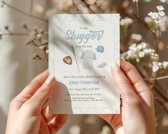 Peut inclure: Une invitation de baby shower sur le thème du baseball. L'invitation présente le texte "A little Slugger is on the way" en bleu clair, avec des illustrations de baseball. L'invitation comprend les détails de l'événement.