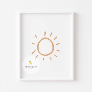 Pu&ograve; includere: Una stampa incorniciata bianca con un semplice sole disegnato a mano in arancione su uno sfondo bianco. La stampa ha un piccolo logo in basso a sinistra che dice "LEMONSODA design".