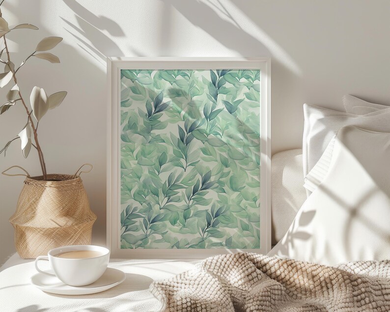 May include: A white framed print with a watercolor design of green and blue leaves on a white background. The print is hanging on a white wall above a bed with white bedding and a brown blanket.