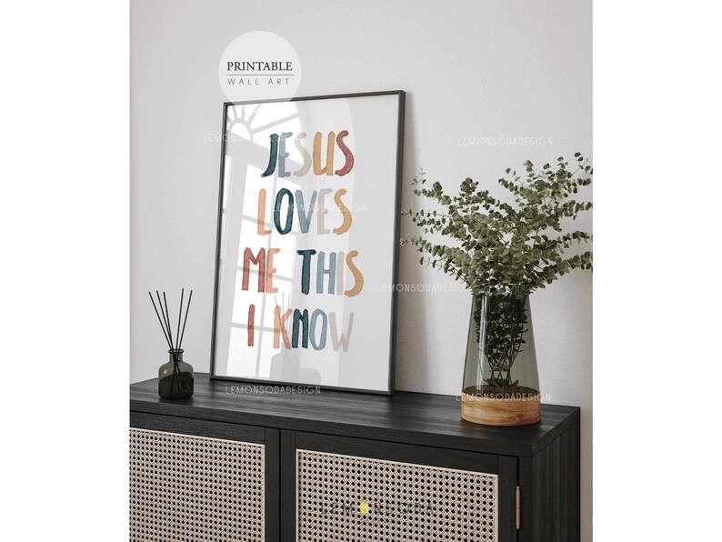 May include: A printable wall art print with the text "Jesus Loves Me This I Know" in colorful, stylized lettering. The background is a watercolor wash of blue, orange, and brown.