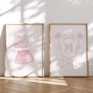 Puede incluir: Dos estampados de rayas rosas y blancas con un atuendo de animadora y un monograma de animadora. El atuendo incluye una blusa y una falda rosa y blanca. El monograma presenta una letra M rosa en un escudo con pompones y un par de bastones de animadora.