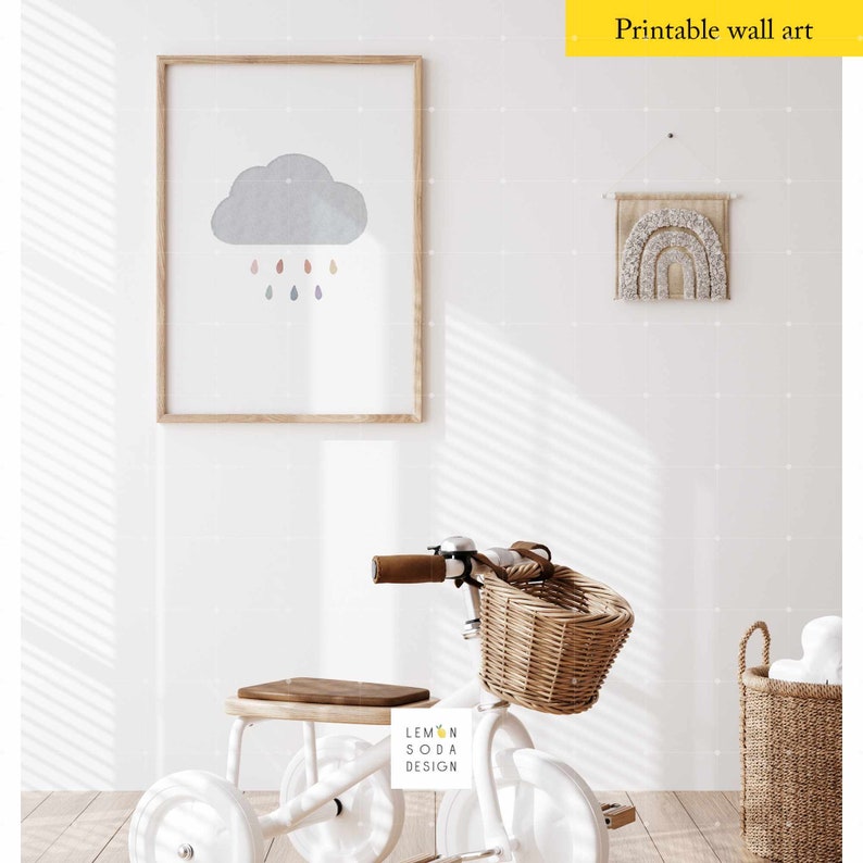 May include: A white tricycle with a wicker basket, a wooden seat, and a brown leather handlebar. The tricycle is in a room with white walls and a framed print of a gray cloud with colorful raindrops. The print is hanging on the wall above a white wooden shelf with a brown wooden seat. There is a woven basket with white items in the corner of the room.