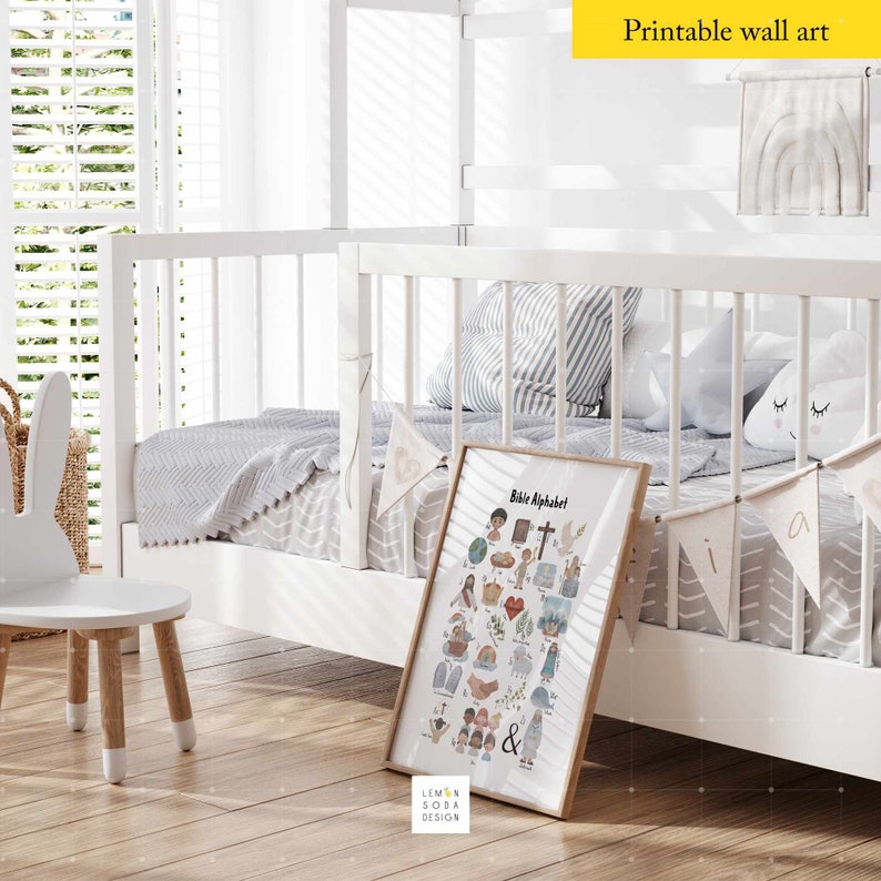 May include: A framed "Bible Alphabet" print with colorful illustrations, displayed in a child's room setting. The room features a white crib, a small chair, and decorative elements. The print is by Lemon Soda Design.