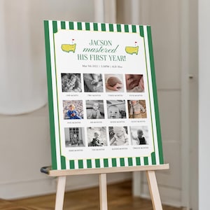 May include: A green and white striped sign on a wooden easel. The sign displays the text "JACSON mastered HIS FIRST YEAR!" with twelve small black and white photos. The sign also includes the date "May 5th 2022" and the weight "6LB 30oz".