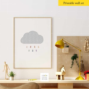 May include: A framed print of a gray cloud with colorful raindrops falling from it. The print is hanging on a white wall above a wooden desk with a yellow lamp, a wooden horse, and a potted plant.