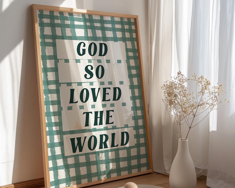 May include: A framed print with a green and white gingham pattern. The print features the text "God so loved the world" in a bold, dark green font.