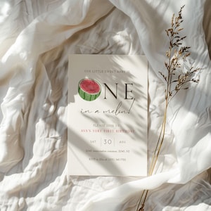 Puede incluir: Una tarjeta de invitación color crema con el texto "OUR LITTLE SWEET BABY IS ONE in a melon!" y una ilustración de acuarela de sandía. La tarjeta también incluye detalles para una fiesta de primer cumpleaños.