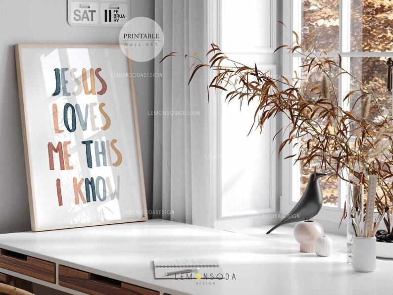 May include: A framed print with the text "Jesus Loves Me This I Know" in colorful, stylized lettering. The background is a watercolor-like design with shades of blue, orange, and brown.