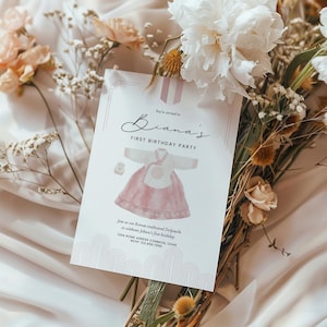 Peut inclure: Une carte d'invitation rose et blanche pour un premier anniversaire. La carte présente une illustration aquarelle d'une robe traditionnelle coréenne, un ruban rose et le texte "You're invited to Diana's First Birthday Party". La carte comprend également le texte "Join us as we celebrate Diana's first birthday with our Korean traditional Doljanchi" et des coordonnées.