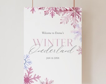 May include: A white poster with a winter theme, featuring watercolor snowflakes in shades of pink and purple. The text reads "Welcome to Emma's WINTER Onederland" with a date below. The poster is suspended by two thin, copper-coloured strings.