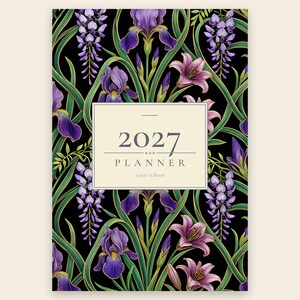 May include: A 2027 planner with a black cover featuring a repeating pattern of purple irises, lilies, and wisteria vines with green stems. A central cream-colored rectangular label displays the text 2027 PLANNER and a year in bloom.