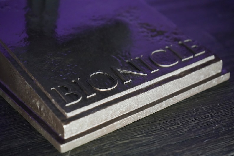 May include: Close-up of a dark gray metal plaque with the word "BIONICLE" engraved in the surface.