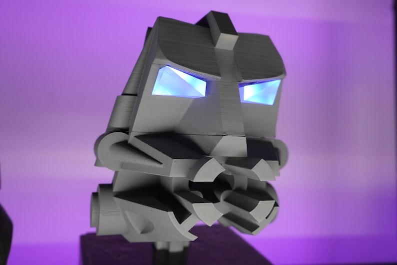 May include: A gray, geometric robot head with blue glowing eyes. The robot head is made of plastic and has a detailed design.