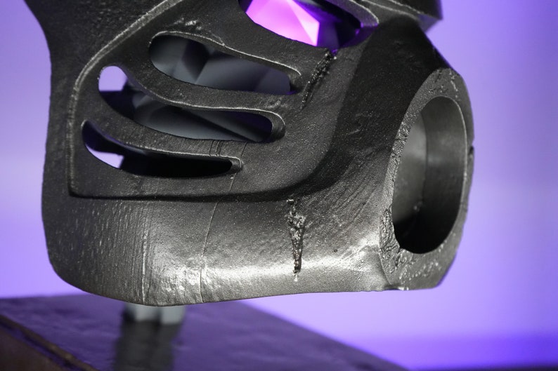 May include: Close-up of a silver-colored 3D printed helmet with a large circular opening on the side. The helmet has a textured surface and appears to be made of plastic.